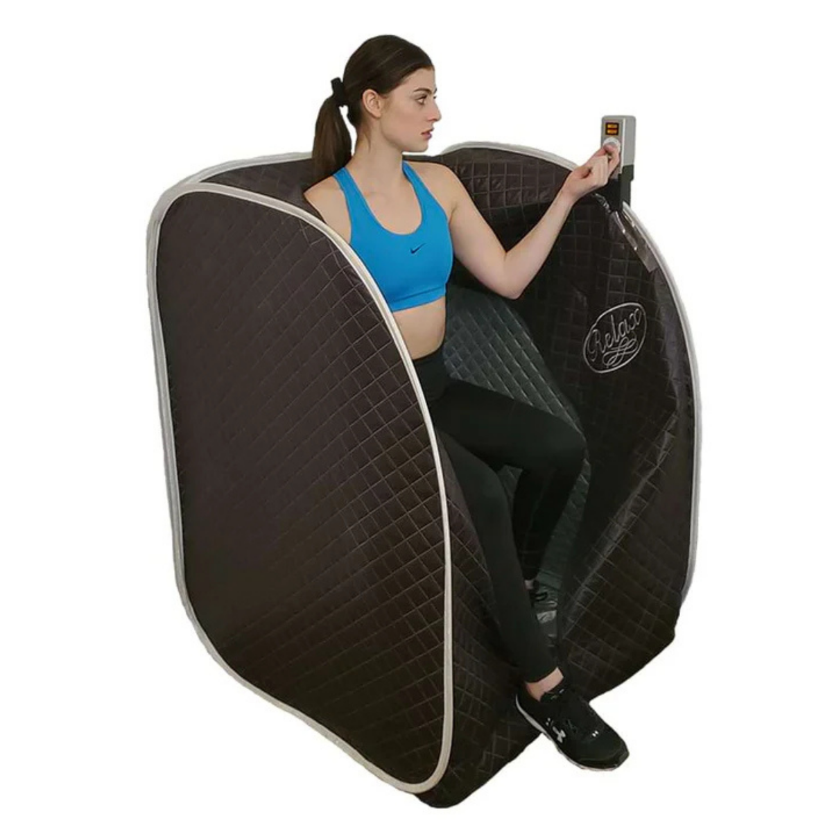 A woman sits inside a dark brown quilted portable infrared sauna tent, holding a control panel. The product is shown on a clean white background.