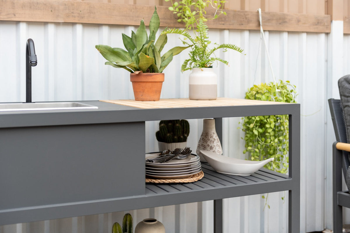 Outdoor kitchen counter with plants, sink, and various items against a white wall.