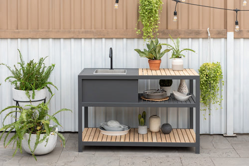 Outdoor kitchen island with sink and shelves, surrounded by potted plants.